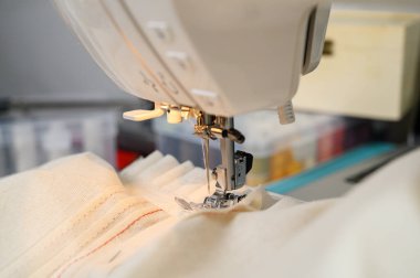 Neredeyse tamamlanmış bir bluza ince dikişler atan dikiş makinesinin makro görüntüsü. Görüntü, iplik etkileşimini, kumaş ayrıntılarını ve giysi montaj anını yakalar. 