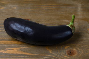 Kırsal bir ahşap masada duran taze, koyu mor bir patlıcan. Yumuşak doğal ışık, pürüzsüz cildini ve kıvrımlı şeklini vurgular ve minimum ve organik bir hayat yaratır.. 