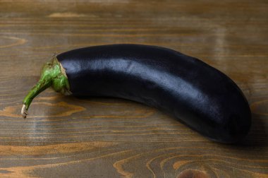 Yıpranmış ahşap bir masanın üzerinde duran koyu mor bir patlıcanın detaylı bir görüntüsü. Derinin dokusu ve ahşabın doğal tanecikleri dokunaklı ve durgun bir hayat yaratır.. 