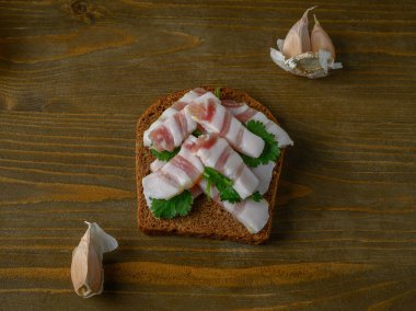 Eski ahşap bir yüzey üzerinde sunulan açık yüzlü koyu çavdar ekmeği dilimlenmiş domuz yağı (salo) ile cömertçe kaplanmıştır. Dokuların zıtlığına ve geleneksel ve dürüst lezzetlere odaklanır..