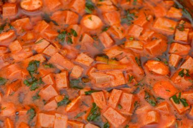 Yumuşak mercimek ve leziz sosis dilimleriyle dolu sıcak, kalın bir domates çorbası. Yakın plan çekimde çekilmiş. Bu tatmin edici yemeğin kırsal dokusunu, zengin rengini ve ev tarzı konforunu vurgular. 