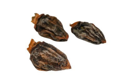 Parlak beyaz bir arka planda üç kuru, çiğnenmiş hurma. Zengin turuncu-kahverengi renklerini, buruşuk yüzeylerini ve sağlıklı sadeliğini sağlıklı ve geleneksel bir tedavi olarak yakalar..