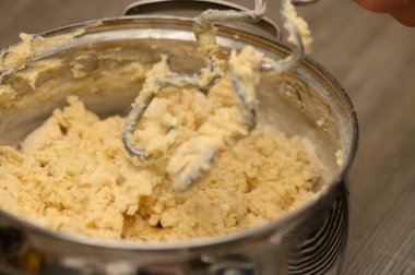 Dinamik bir mutfak sahnesi, bir el çırpma makinesinin, kalın Stollen hamuru arasında dönüp durduğunu, dokunsal enerjiyi ve bayram pişirmenin şenlikli sıcaklığını yakaladığını gösteriyor..