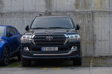 Tiflis, Gürcistan 12.11.2025 Glossy siyah Toyota arazi kruvazörü modern ofis binalarının yakınına park etmiş. Sofistike şehir ortamında engebeli araçların aksine.