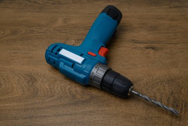 Üzerinde metal matkap bulunan kablosuz matkap, ahşap bir tezgahın üzerine yerleştirilmiş. DIY, atölye veya hırdavatçı konsepti için araç fotoğrafçılığı.
