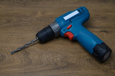 Yıpranmış ahşap masa yüzeyine yerleştirilmiş gümüş matkapla çağdaş kablosuz matkap. Modern araçların ve doğal kırsal arkaplanın zıttı.