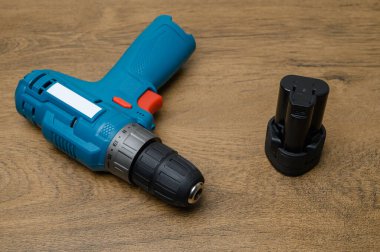 Bataryalı kablosuz matkap parçalanmış ve yıpranmış ahşap masada aletin yanına yerleştirilmiş. Silinebilen güç sistemi ve araç modüleritesine odaklan.