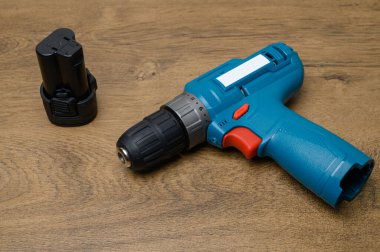 Profesyonel kablosuz matkap pili kısmen çıkarılmış, bağlantı terminalleri yaşlanmış ahşap tezgahta görünüyor. Donanım resimlemesi için teknik araç fotoğrafçılığı.