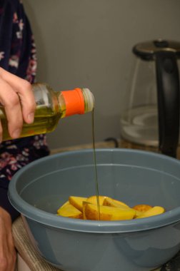 Baharat ve pişirmeden önce gri bir seramik kasede şişeden taze patates dilimlerine dökülen pişirme yağına yakın plan. Ayrıntılı yemek hazırlama anı.