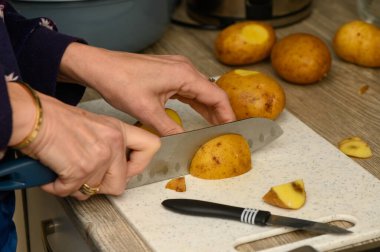 Mavi saplı mutfak bıçağı kullanarak sarı patatesleri beyaz kesim tahtasına tam olarak dilimlemek için detaylı bir yakın çekim. Kesme tekniğine ve taze malzemelere odaklan..