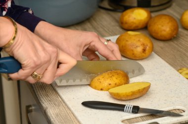 Mavi saplı bıçak, beyaz kesme tahtasındaki taze sarı patatesi delip geçiyor. Doku ve hassasiyete odaklı keskin mutfak aksiyon fotoğrafçılığı.