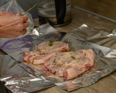 İki çiğ domuz filetosu kremalı hardal ya da yağ bazlı terbiye ve taze biberiye filizleri ile tatlandırılmış, pişirmeye ya da ızgara yapmaya hazır alüminyum folyonun üzerinde dinleniyor..