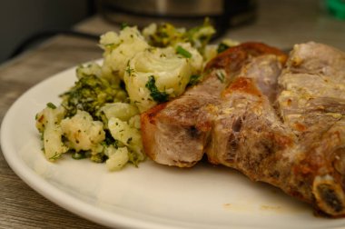 Haşlanmış ya da kaynatılmış karnabahar ve brokoli parçalarıyla servis edilen aşırı yakın plan altın sarısı domuz pirzolası. Ayrıntılı yemek dokusu fotoğrafçılığı.