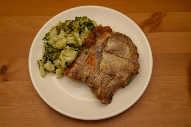 Yemek tabağında brokoli ve karnabahar çiçekleriyle servis edilen kızarmış domuz pirzolası. Basit yemek kompozisyon fotoğrafçılığı.