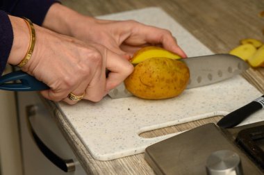 Eller temiz kesiyor, patatesleri tertemiz beyaz plastik bir kesme tahtasının üzerinde kırsal takozlar haline getiriyor. Bu resim, ev yapımı yemek için taze malzemeler hazırlamanın basitliğini vurgular..
