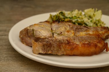 Kırsal bir mutfak masasında hazırlanmış, kavrulmuş sebzeli karnabahar ve brokoli karışımının yanında altın çıtır domuz pirzolası servis ediliyor. Samimi ev yapımı akşam yemeği fotoğrafçılığı..