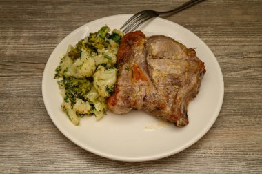 Mükemmel pişirilmiş kemikli domuz bifteği aromatik bitki ve baharat kabuğuyla servis ediliyor, el değmemiş beyaz tabakta servis ediliyor. Et kalitesine odaklanan minimalist mutfak sunumu.