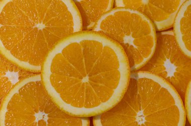 Yeni dilimlenmiş portakal dilimlerinin yukarıdan aşağıya yakın çekimi canlı ve dokulu bir arka plan oluşturuyor. Görüntü parlak turunçgiller, parlak renkler ve meyve dilimlerinin tekrarlayan geometrik desenlerine odaklanıyor..