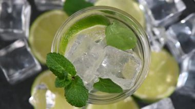 Mojito büyüsü. Üst aşağı dönen kokteyl bardağı koyu arka planda. Sinematik makro çekim.