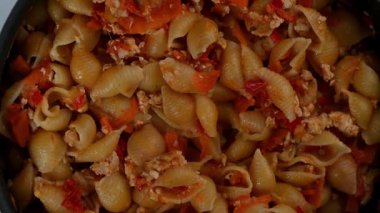 Pişmiş kabuklu makarnanın (conchiglie) lezzetli bir 4K yukarıdan aşağıya video döngüsü, baharatlı et ve canlı sebzelerle servis edilir ve yavaş yavaş tabakta döner. Klip renkli kompozisyonu vurgular