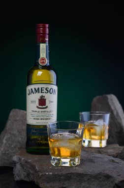 01.02.2026 Tiflis, Gürcistan tarzı kompozisyonda bir şişe Jameson Irish viskisi ve yanında zengin yeşil bir zemin üzerine yerleştirilmiş buzla dolu iki viski bardağı bulunuyor. Rahatlatıcı, kaliteli bir içme ortamı yaratıyor.