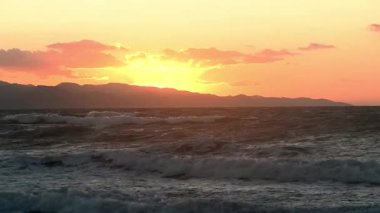 Kuzey Kıbrıs KKTC 'nin Akdeniz kıyısında günbatımının çarpıcı panoramik manzarası. Kompozisyonda sahile yuvarlanan sakin turkuaz deniz dalgaları ve dramatik silueti yer alıyor.