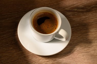 Bir fincan aromatik Türk kahvesi yumuşak dramatik ışıklandırmayla ahşap yüzeyde güzelce sunuluyor. Sıcak atmosferli kültürel içecek kavramı.