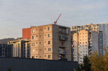 Parlak güneş ışığıyla aydınlatılan çok katlı modern binalar. Mimari formlar ve bina cepheleri dinamik şehir manzarası yaratır..