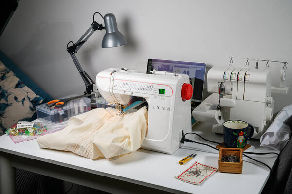 An intimate, well-loved sewing corner featuring a vintage sewing machine, a functional overlocker, and handmade tools like pincushions and scissors. Warm lighting and wooden surfaces create a nostalgic, craft-focused atmosphere.