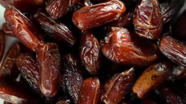 Tertemiz bir 4K video döngüsü. Kurumuş tatlı tarihler, yukarıdan aşağıya doğru bir perspektiften, karanlık bir yüzeyde düzgün bir şekilde dönüyor. Klipsi parlak, yapışkan yüzeyi, koyu kahverengi rengi ve kırışıklığı vurgular.