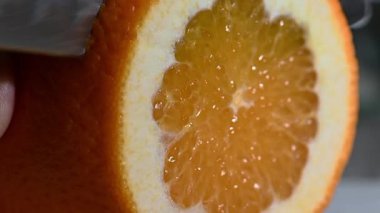Keskin bir bıçakla keskin bir portakalı temiz yapmak için bir şefin maharetli ellerini yakın plan çekimleri, hatta koyu bir tahta üzerinde takozlar. Bıçak ve yiyeceğin üzerinde meyve suyu parlıyor. Keskinliğe, tazeliğe ve renklerin parlak kontrastına odaklan