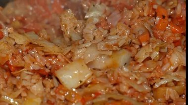 Domates soslu tavada usulca kaynayan domuz eti ve pirinçli yumuşak lahana. Havuç ve soğan ekliyor, tatlı, buhar yükseliyor, yumuşak doku. Ev yapımı yemekler, Doğu Avrupa konforlu yemekler. Yakın çekim, sıcak mutfak ışığı.