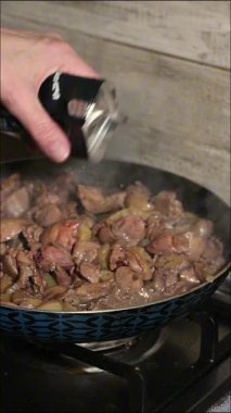 Sıcak tavada pişen taze tavuk ciğeri üzerine karabiber öğüten bir şefin yakın plan fotoğrafı. Biber düştükçe buhar yükselir ve yemeğe aroma ve tat katar. Otantik, profesyonel pişirme sürecini yakalar. Mükemmel.