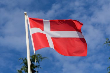 Danimarka 'nın canlı kırmızı ve beyaz ulusal bayrağı bulutlarla dolu açık mavi bir gökyüzünün altında dalgalanır..