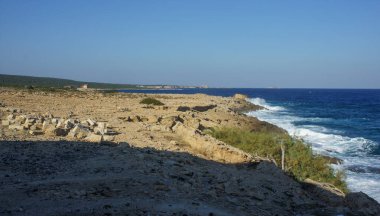 Dalgalar açık mavi gökyüzünün altındaki kayalara çarptığında engebeli kıyı şeridi masmavi denizle kesişiyor..