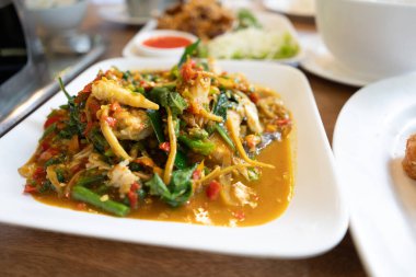 Beyaz kare tabakta, yeşil sebzeli, altın-kahverengi soslu, baharatlı Tayland kızartması var..