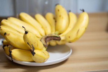 Olgun, sarı küçük muzlar tahta bir yüzey üzerinde beyaz bir tabakta dinlenirler..