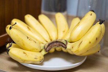 Olgun, sarı küçük muzlar tahta bir yüzey üzerinde beyaz bir tabakta dinlenirler..