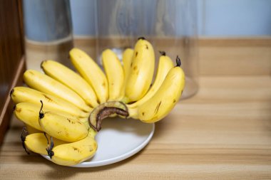 Küçük bir demet olgun, sarı muz, tahta bir yüzey üzerinde beyaz bir tabakta duruyor..