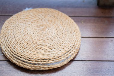 Yuvarlak dokuma hasırı ya da sarmal dokusu olan bardak altlığı ahşap bir masada oturur..