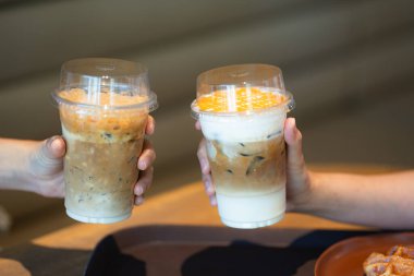 İki el, sütlü ve karamel katmanlı buzlu kahve içecekleriyle kadeh kaldırıyor..