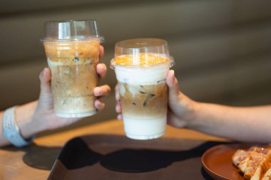 İki el, sütlü ve karamel katmanlı buzlu kahve içecekleriyle kadeh kaldırıyor..