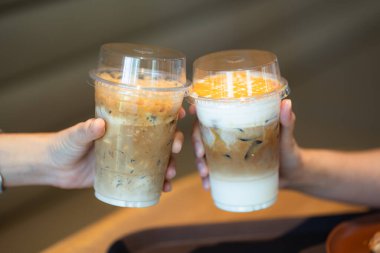 İki el, sütlü ve karamel katmanlı buzlu kahve içecekleriyle kadeh kaldırıyor..