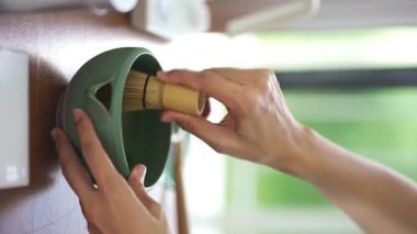 Geleneksel bambu çırpıcı kullanarak seramik bir kasede parlak yeşil kibrit çayı çırpıyor..