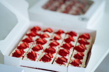 Dilimlenmiş kırmızı kadife kek kareleri ve tohum kaplı muffinlerle dolu beyaz kutuların yer aldığı gurme yemek servisi..