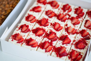 Dilimlenmiş kırmızı kadife kek kareleri ve tohum kaplı muffinlerle dolu beyaz kutuların yer aldığı gurme yemek servisi..