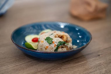 Sebzeli ve limonlu leziz pilav servisi ahşap bir masada mavi bir seramik kasede oturur..