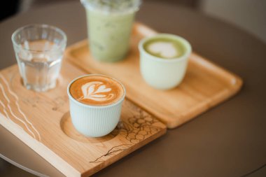 Sıcak latte, buzlu kibrit latte ve su da dahil olmak üzere çeşitli içecekler karanlık masanın üzerindeki ahşap tepsilerde oturur..