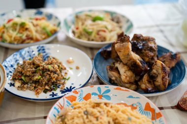 Çeşitli renkli kaseler ve tabaklar erişte, ızgara et ve karışık kızartma tabakları açık renkli bir masanın üstüne dizilir..