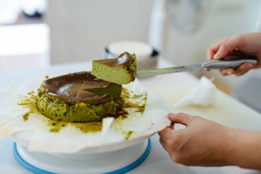 Metal bıçaklı biri, yeşil kibrit kutusundan beyaz parşömen kağıdının üzerinde duran üç köşeli dilimi kaldırıyor..